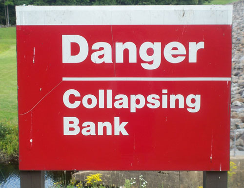 Sign At The Edge Of A Lake Stating Danger Collapsing Bank